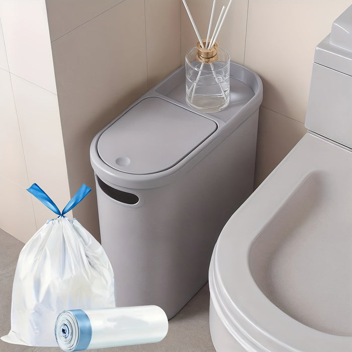 Gray trash bin with a bag and roll next to a toilet in a bathroom setting