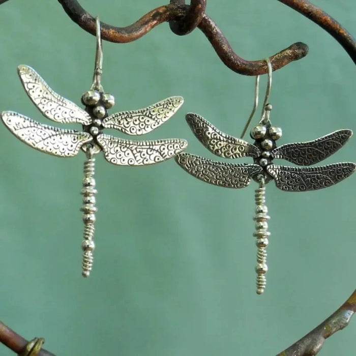 Two silver dragonfly earrings on a green background
