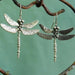 Two silver dragonfly earrings on a green background
