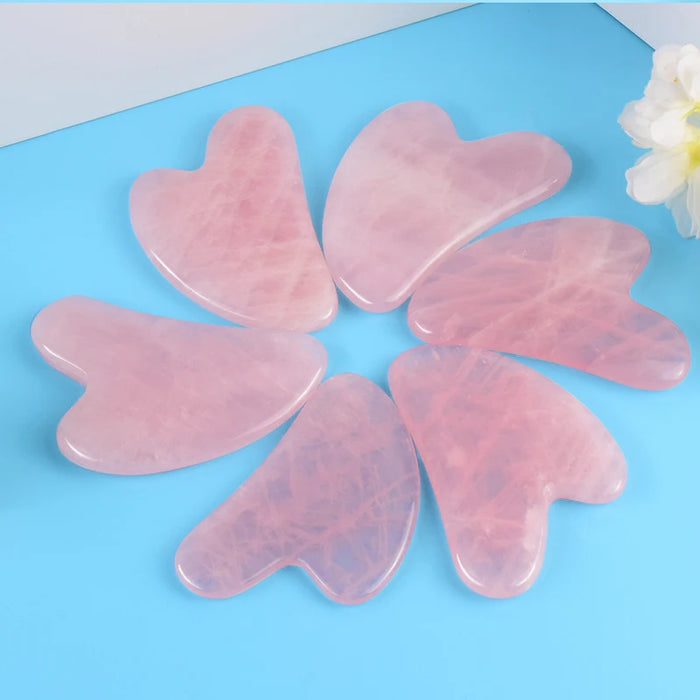 Six pink heart-shaped gua sha tools on a blue background