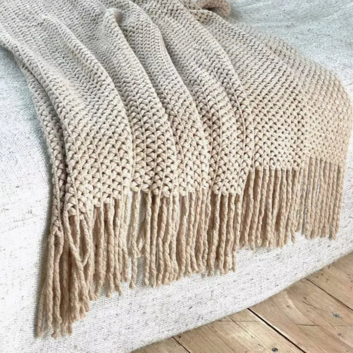 Khaki knitted throw with tassels on a white rug