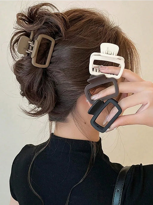 Four square matte claw clips in brown, white and black held beside a twisted updo