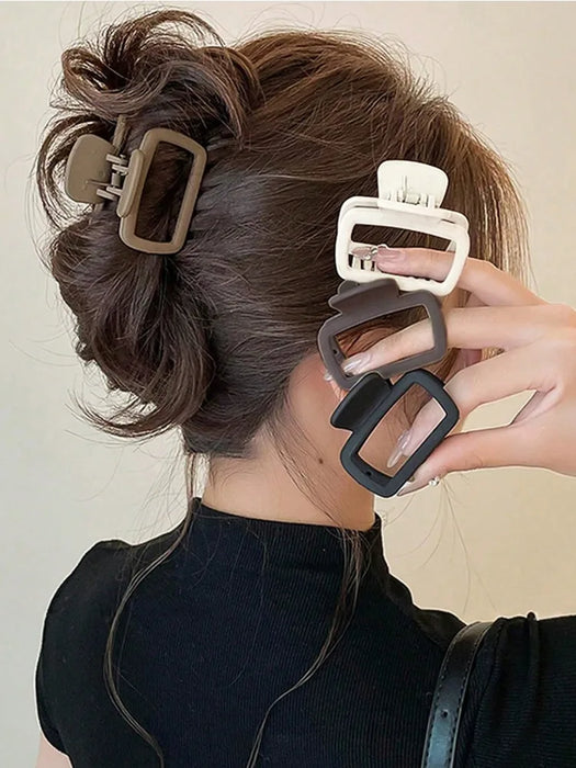 Four square matte claw clips in brown, white and black held beside a twisted updo