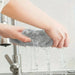 Hands wringing water from a grey microfibre cloth over a sink