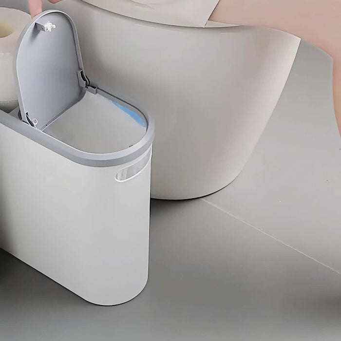 Gray trash can with open lid next to a toilet in a bathroom setting